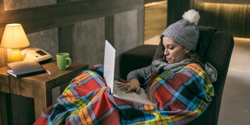 women on couch wrapped in blanket and reading a book