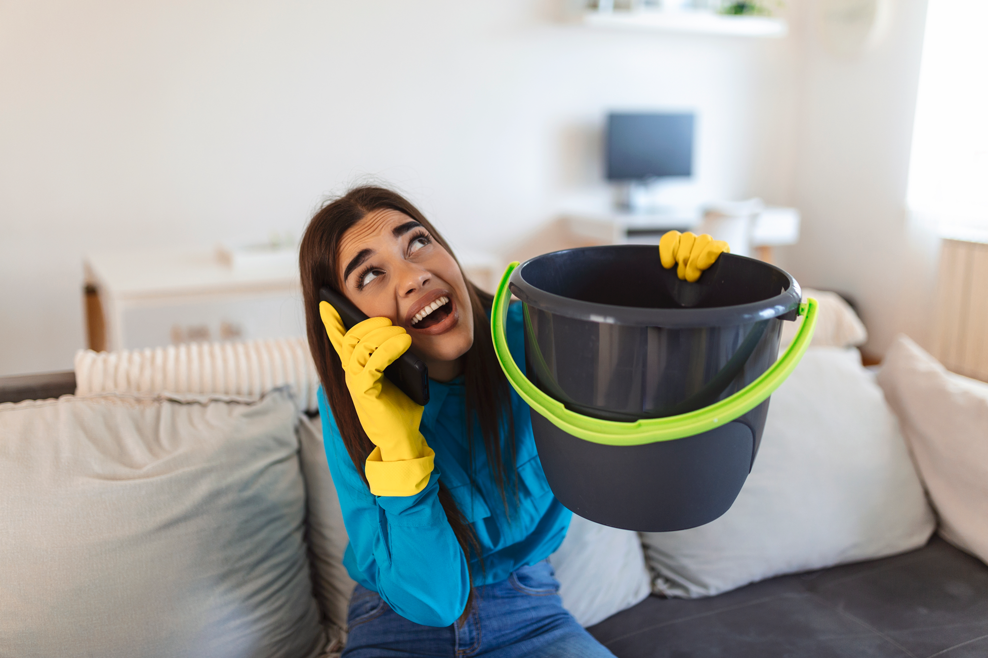 A woman holding a bucket to prevent the plumbing leak from the ceiling